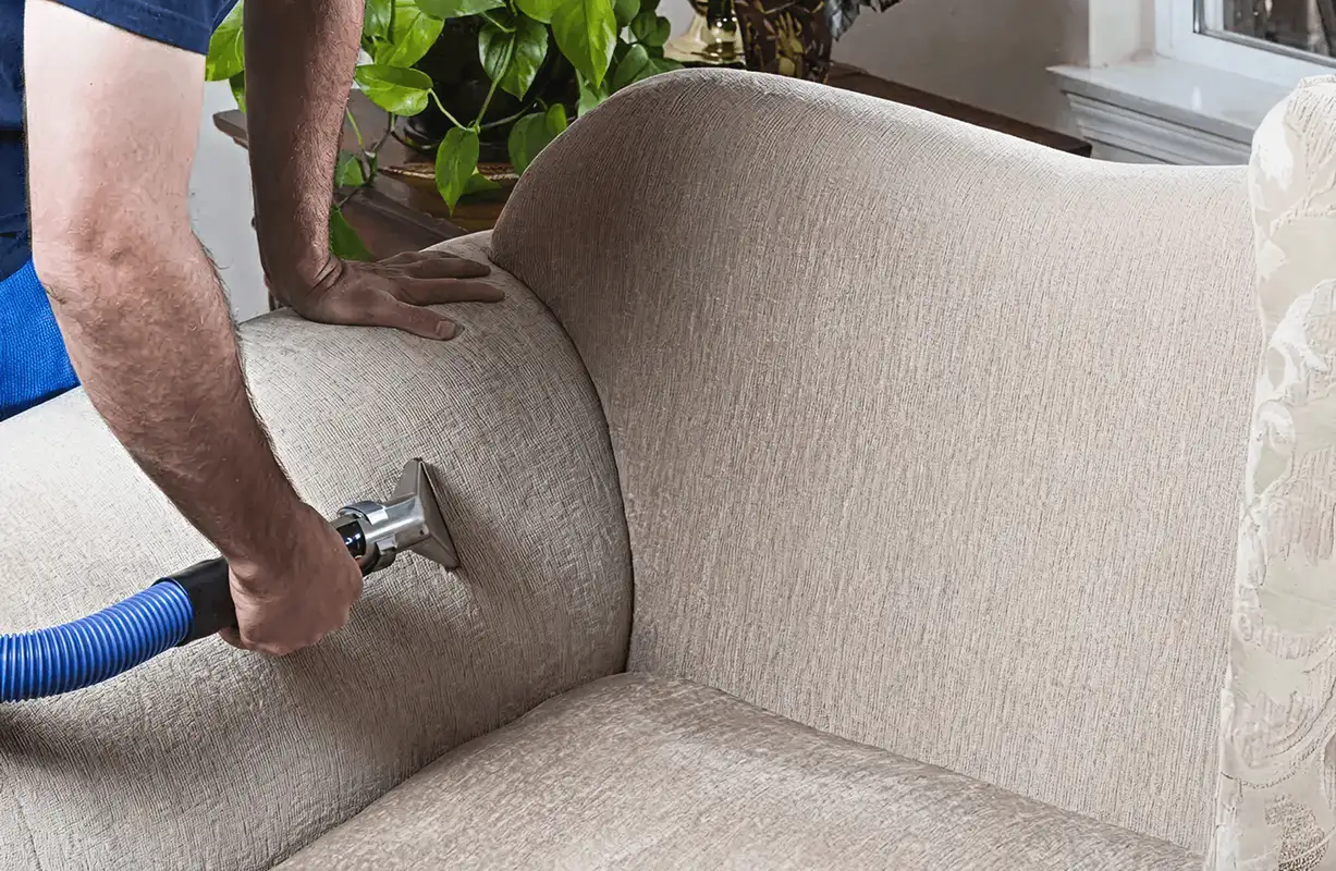 Professional upholstery cleaner deep-cleaning a fabric sofa with a handheld extraction tool and hose, Glendale, AZ.